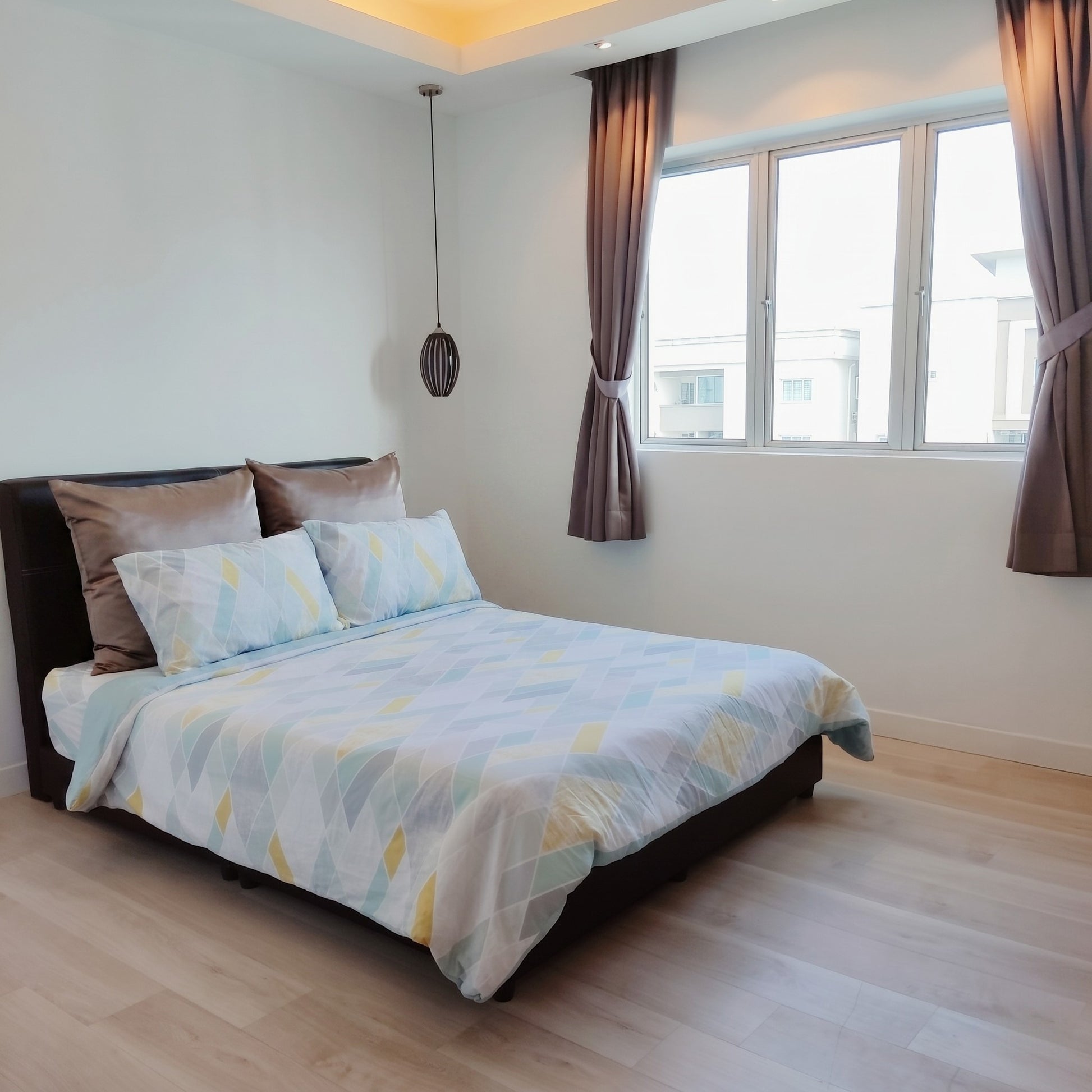 Bedroom with a bed featuring a patterned comforter and pillows, wooden floor, and large window.