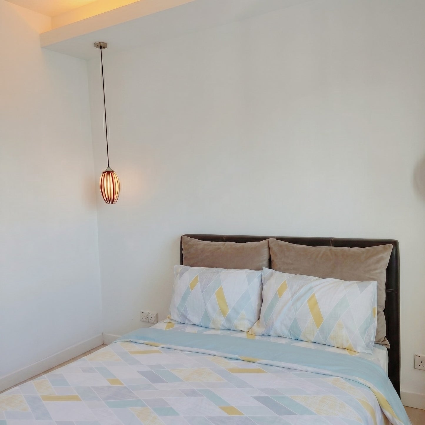 Bedroom with a bed featuring a patterned comforter and pillows, under a hanging light fixture.
